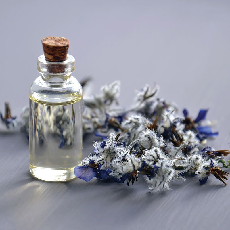 Small glass bottle with cork beside blue and white dried flowers on a gray surface