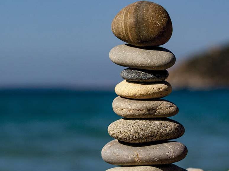 Stacked smooth stones balanced on a beach with the sea and sky in the background