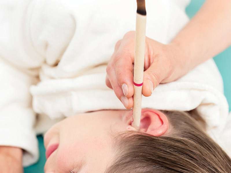 Hand placing a pencil near a child's ear, suggesting an ear exam on a white towel background