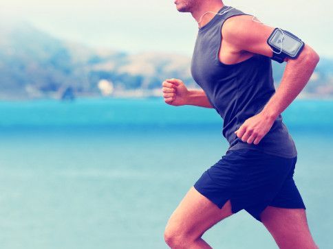 Runner in black athletic wear jogging by a blue waterfront with a smartphone armband