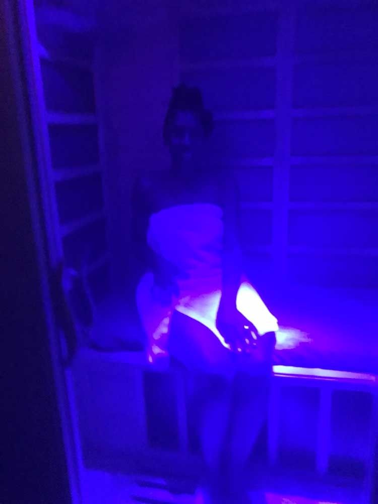 Person in purple-blue light holding a glowing object inside a dark room or corridor.