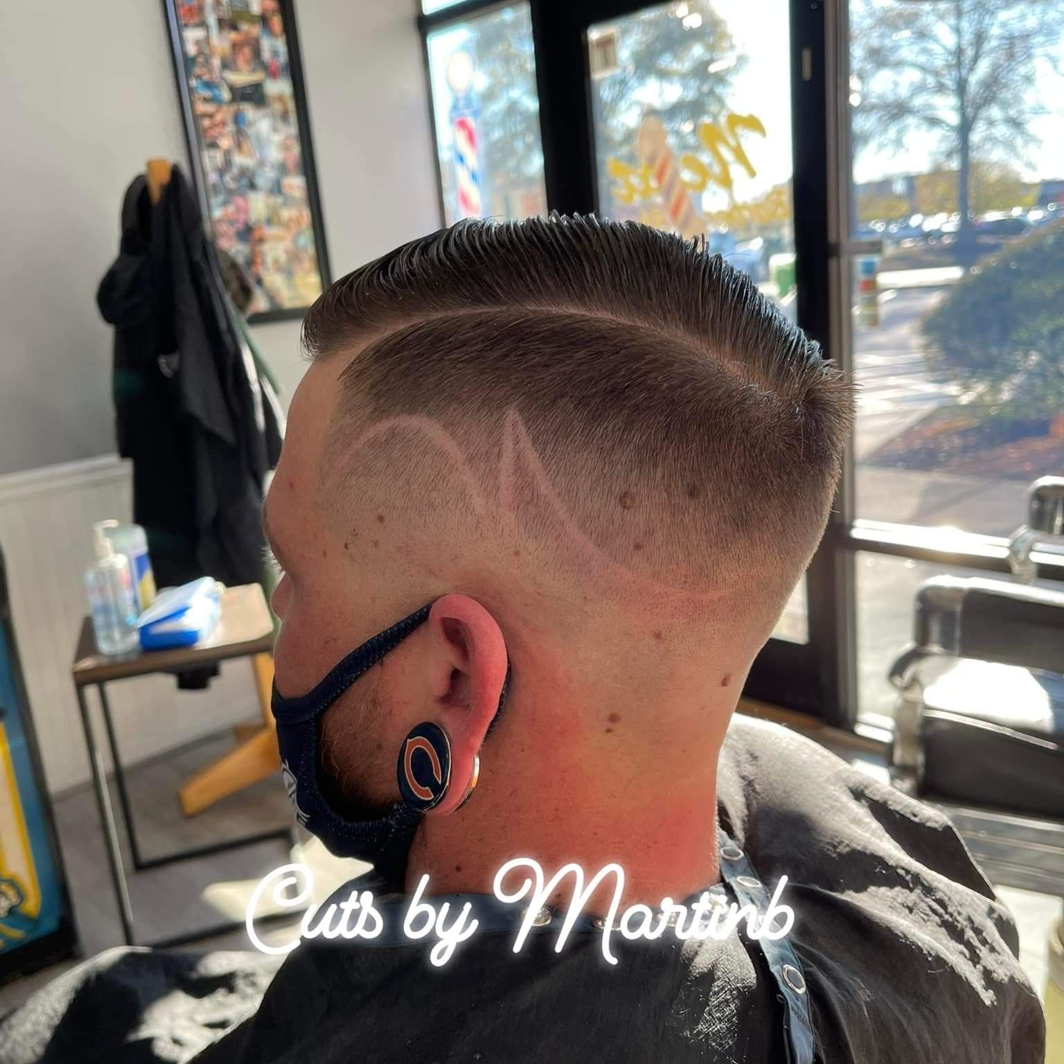 A profile view of a sharp, faded haircut with a side part and a subtle hair design, set inside a barbershop.