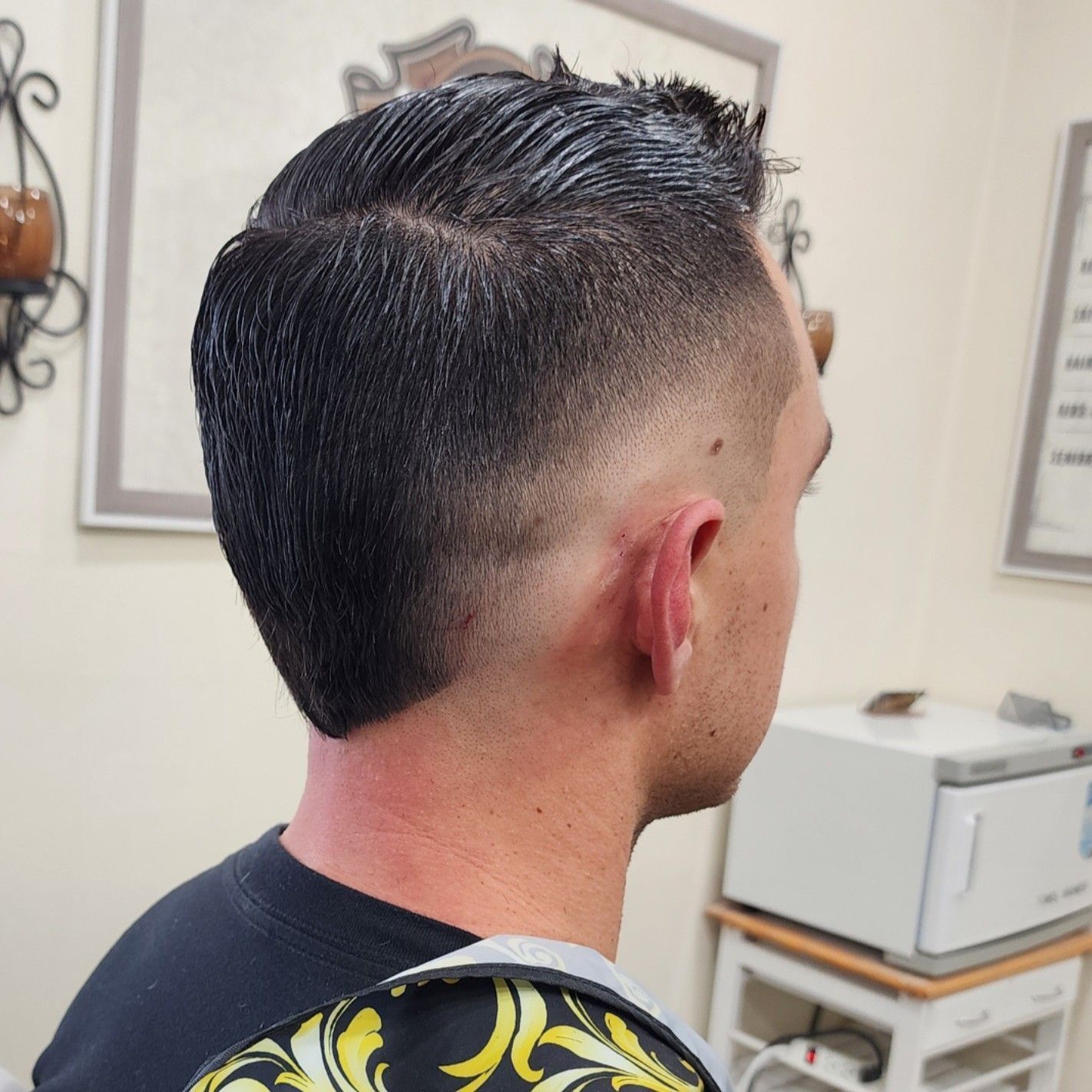 A side-view of a short, dark-haired mohawk haircut with a precise skin fade, styled in a salon setting.