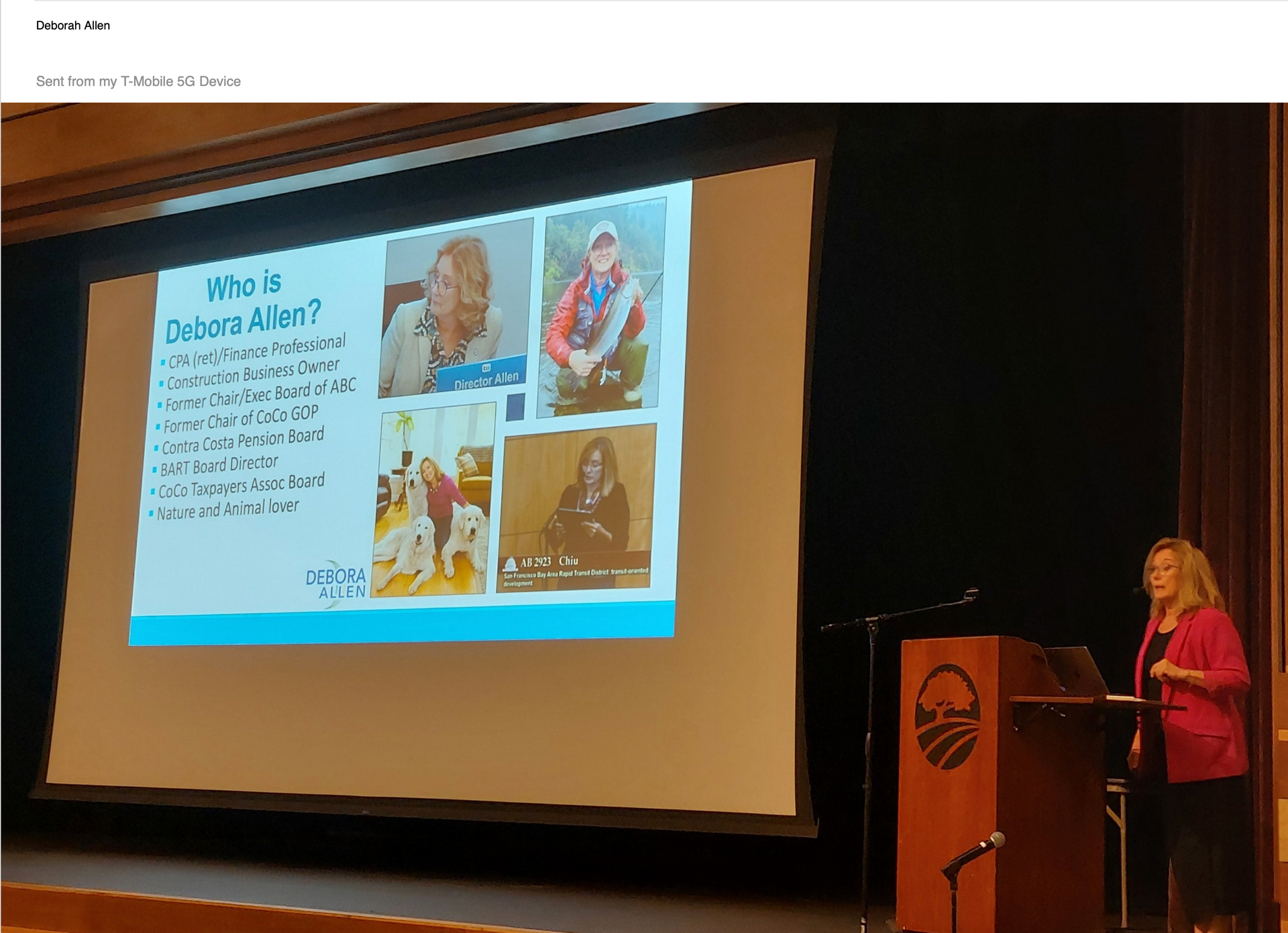Speaker presenting slide at podium in a lecture hall, with photos displayed on a large screen.