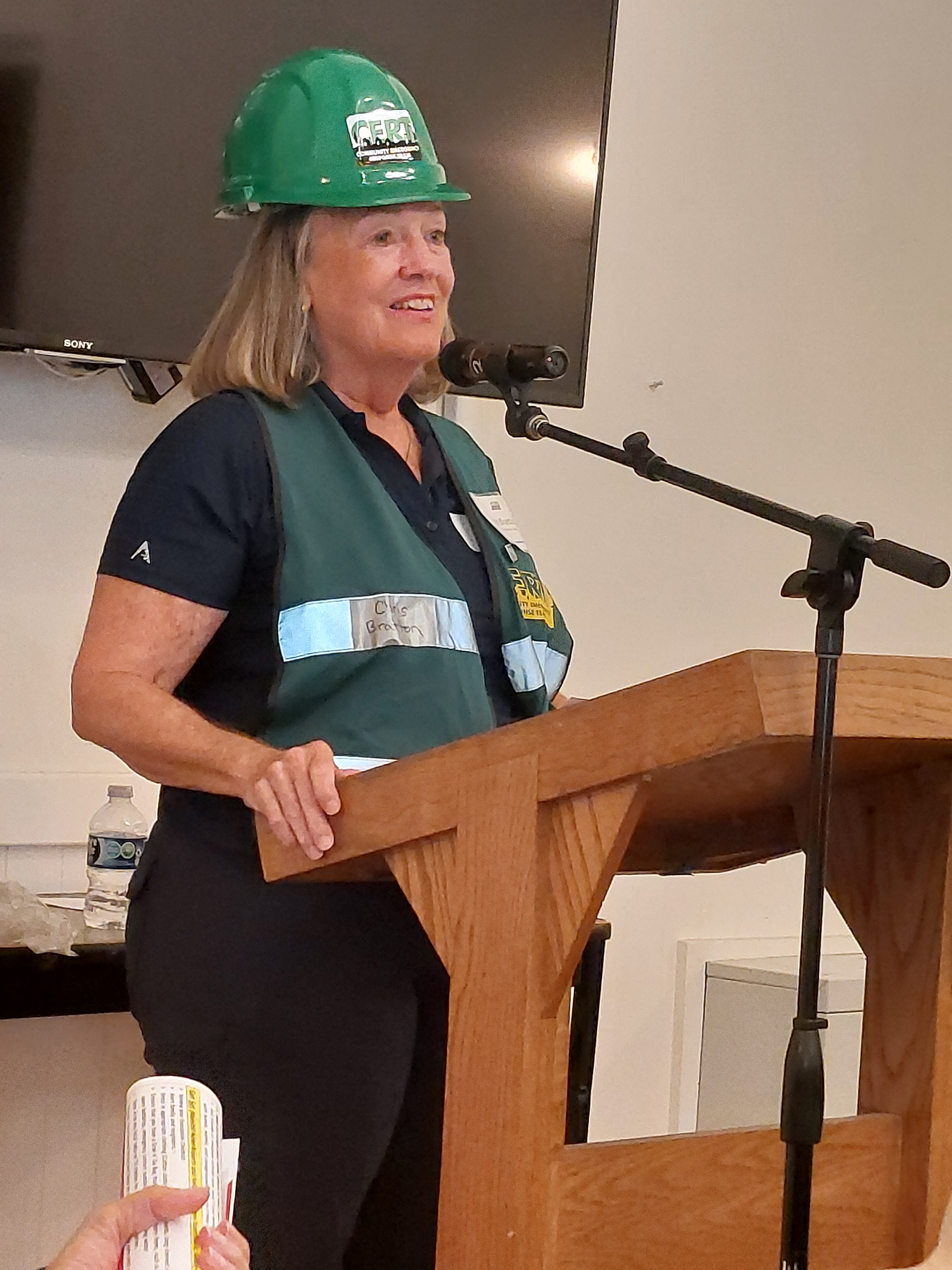 Woman in a green hard hat speaking at a podium with a microphone indoors