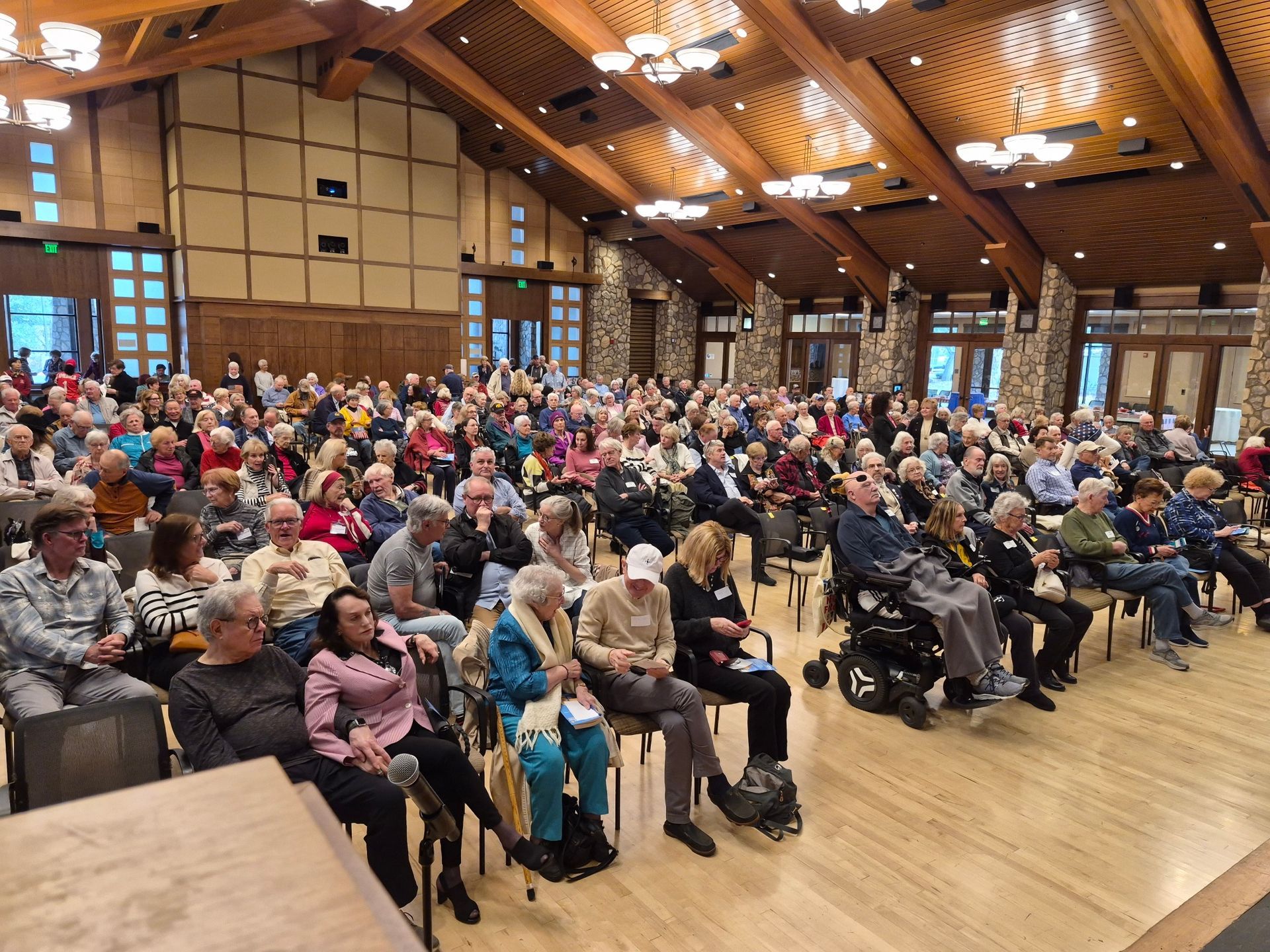 Crowded community hall with seated audience in a wooden auditorium, watching an event.