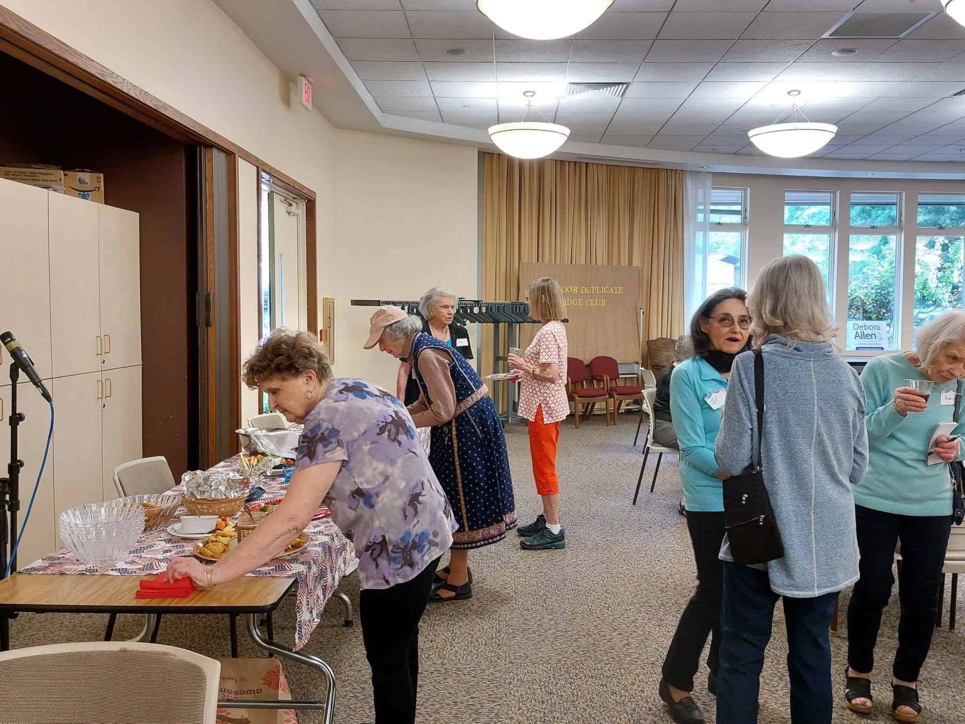 People browsing tables and hanging clothes in a bright community room with windows and curtains
