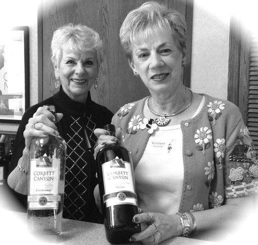 Two women smiling and holding wine bottles indoors