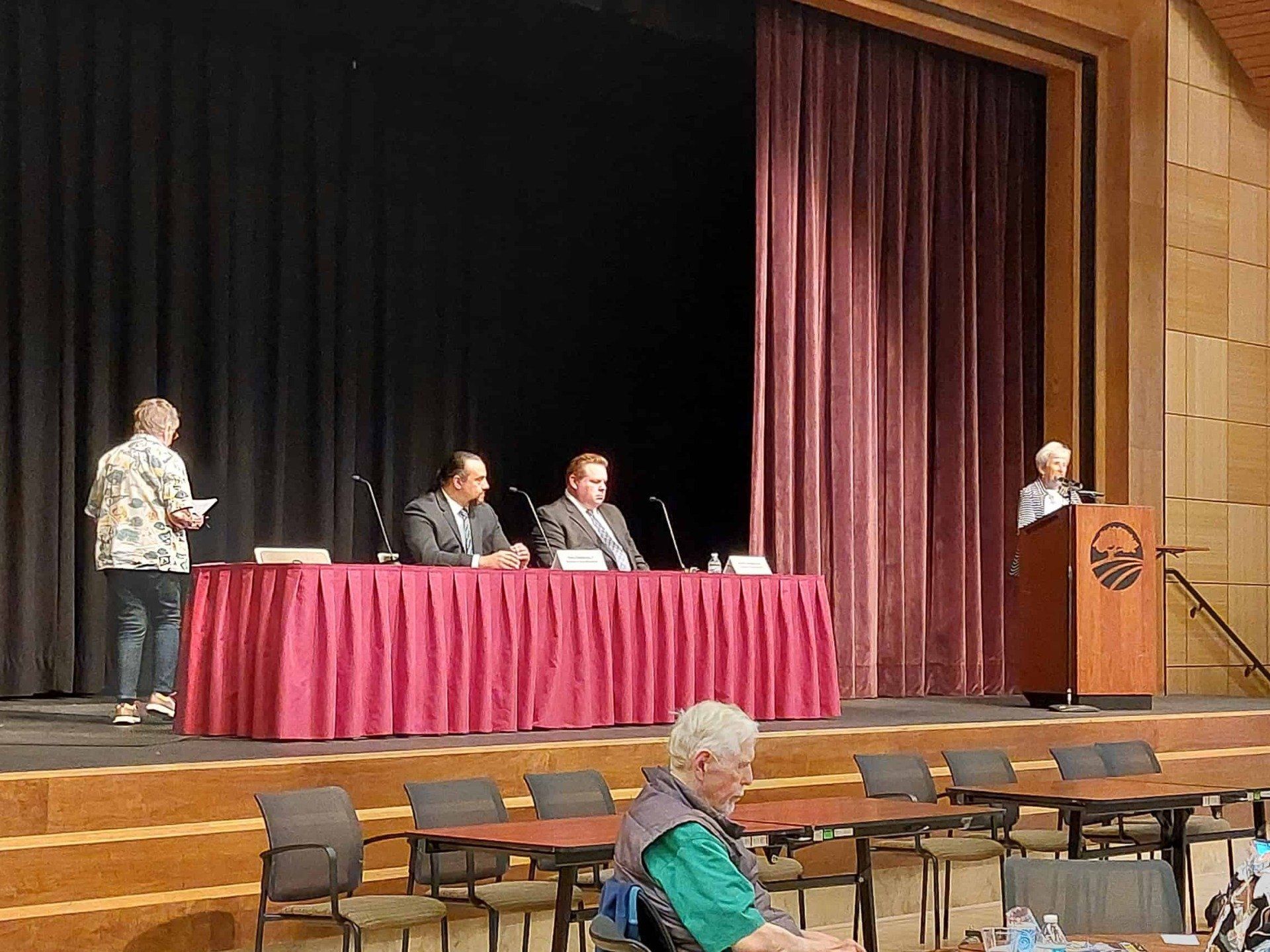 Panel discussion on stage with speakers at a table and podium; audience chairs in foreground
