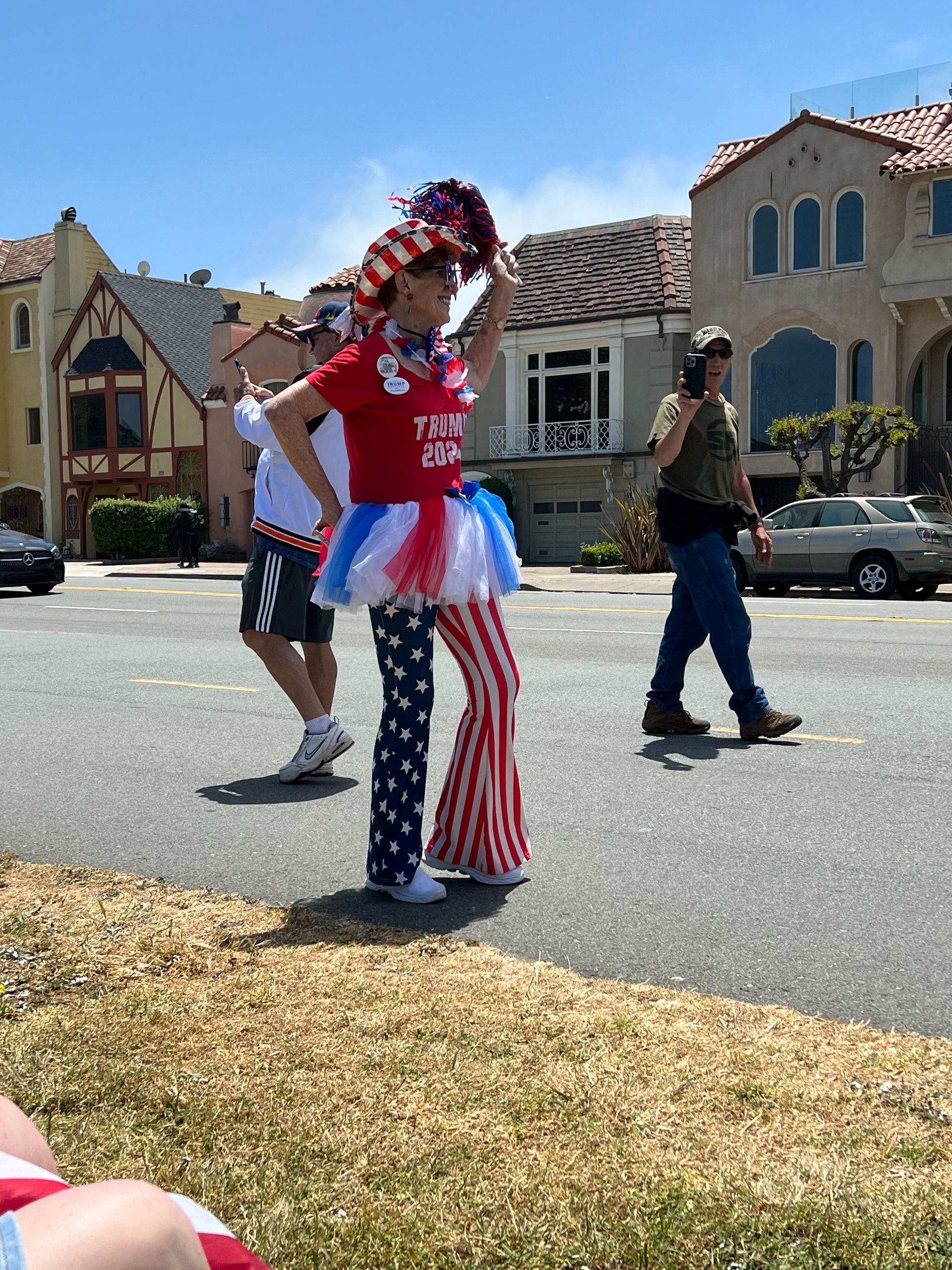 Person in red, white, and blue costume waving in a neighborhood street during a parade