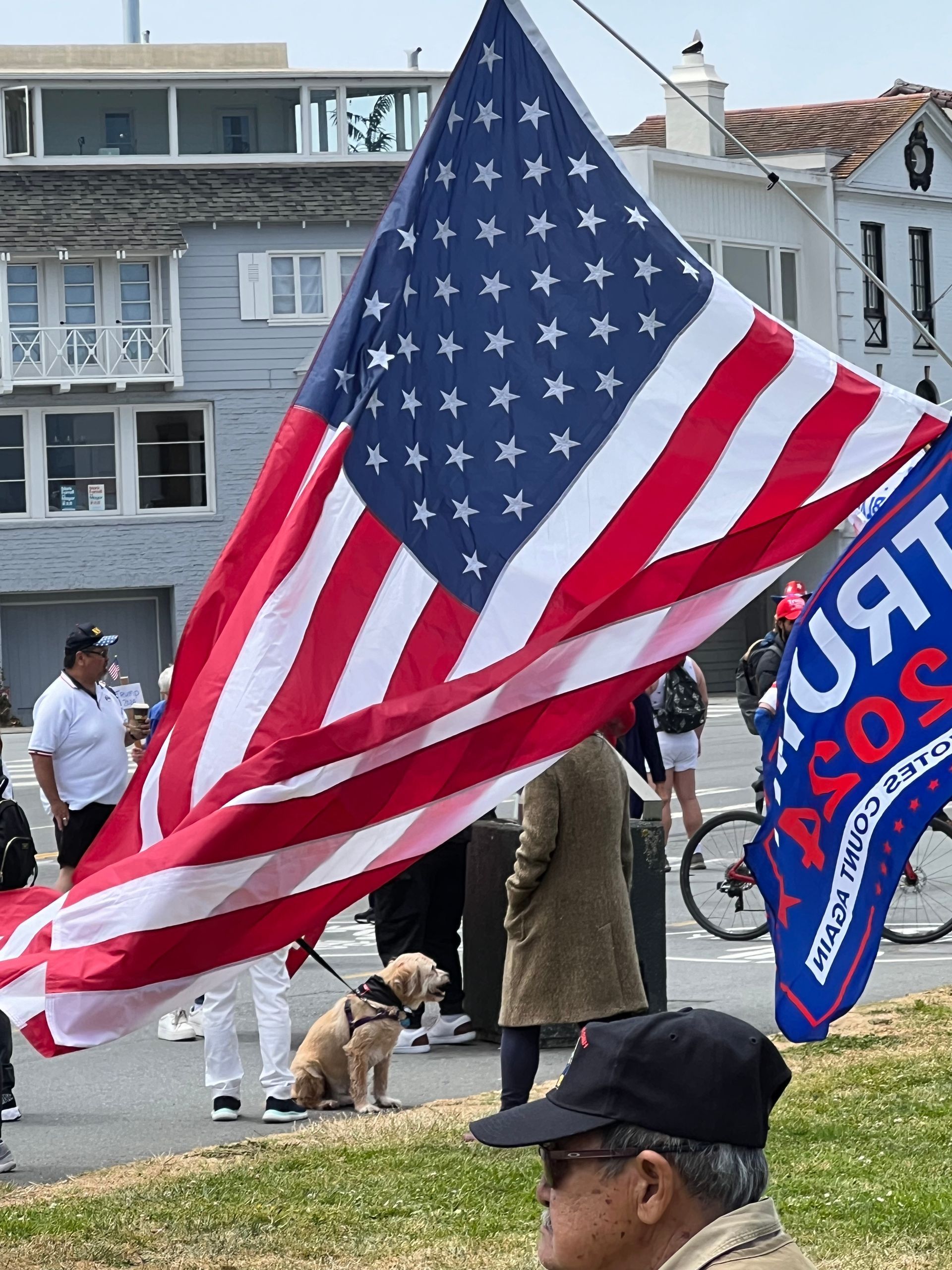 U.S. flag and Trump 2020 campaign flag at an outdoor rally near houses on a waterfront street