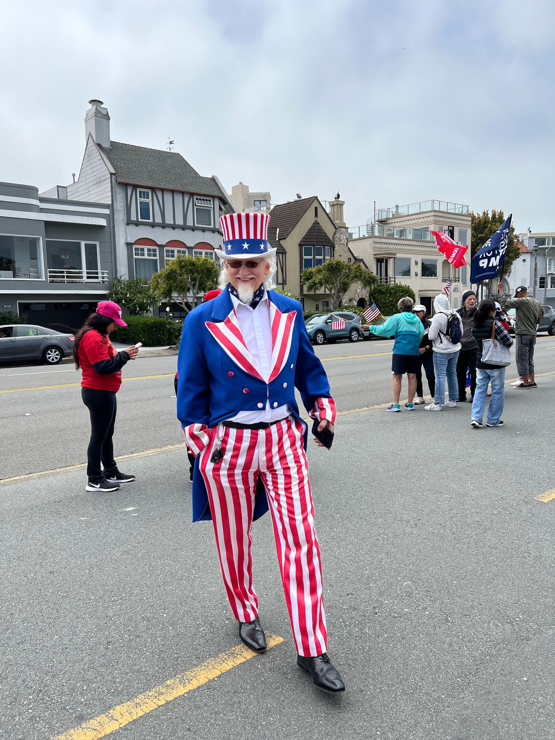 Man in red, white, and blue patriotic outfit standing on a street with spectators and buildings behind him