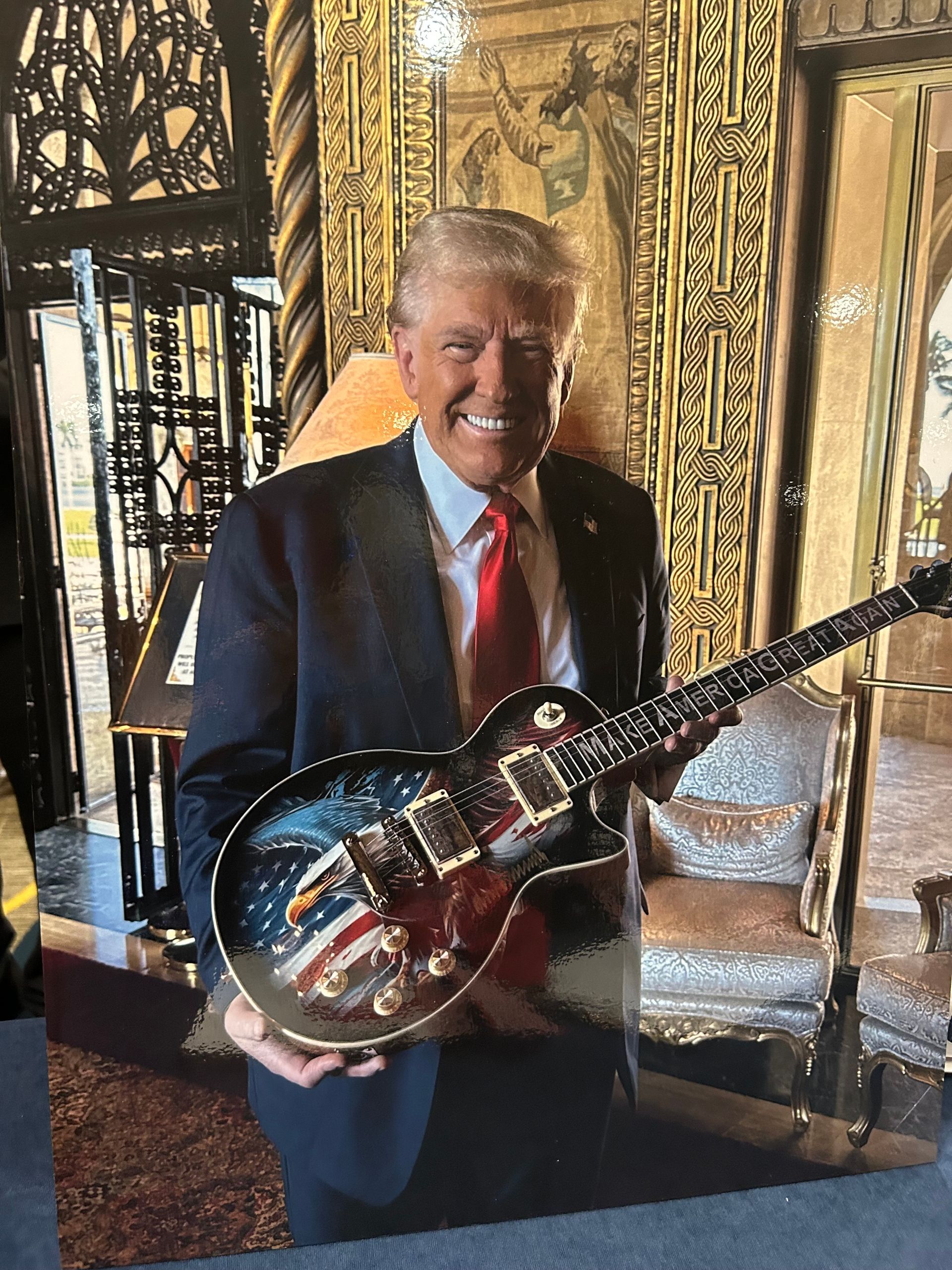 Smiling man in a suit holding a guitar in an ornate, gold-accented room