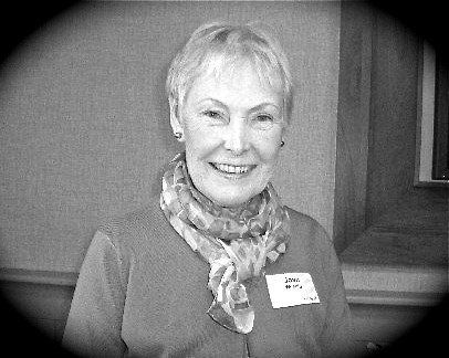 Smiling woman in a scarf and name tag, standing indoors against a plain wall.