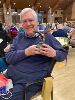 Smiling man in a navy sweater holding a small trophy in a banquet hall