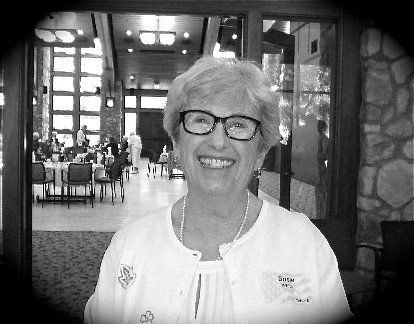 Smiling woman with glasses in a white blouse, standing in a doorway of a restaurant interior.