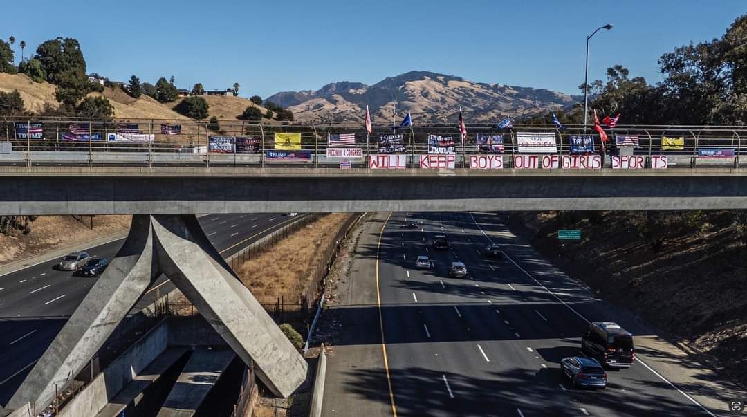 Highway overpass with traffic below and a pedestrian bridge across the road, hills in the background