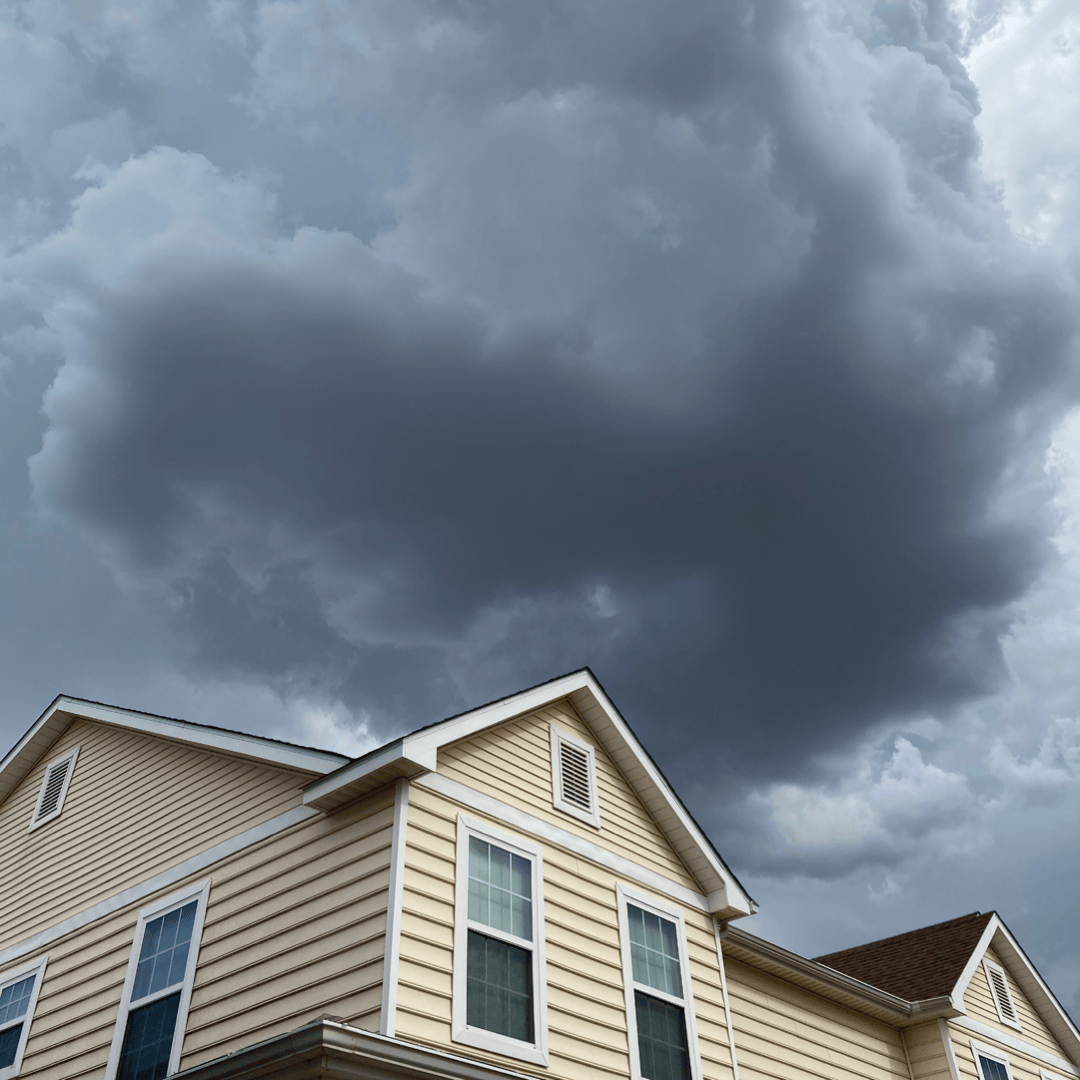 Dark storm clouds looming over the roofline of a beige house