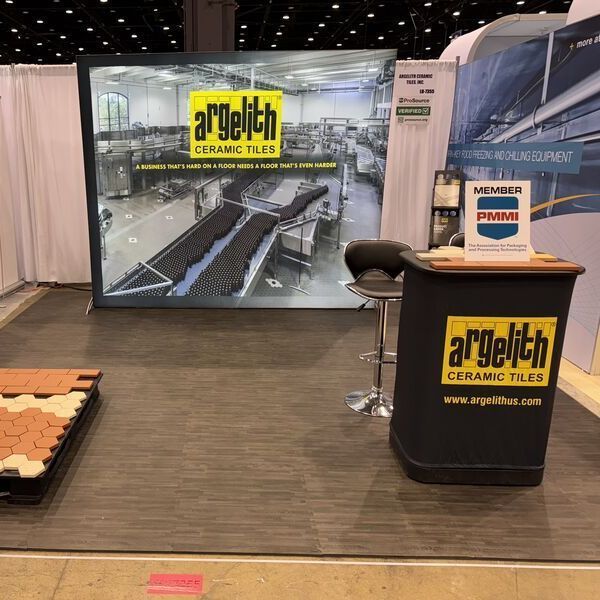 Trade show booth for a’ghell? flooring tiles with black counter, display graphic, and sample panels in a convention hall