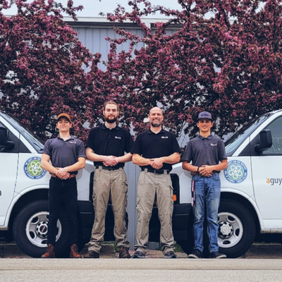 Four people standing between two white service vans in front of a flowering tree