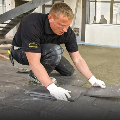 Worker in black shirt and white gloves installing roofing material on a flat roof