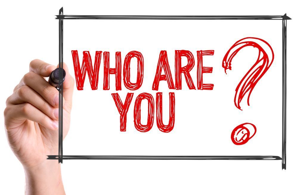 Hand holding a sign that says “WHO ARE YOU?” in red letters with a red question mark