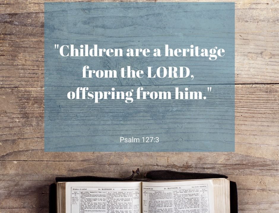 Bible verse on blue paper over a wooden table with an open Bible below.