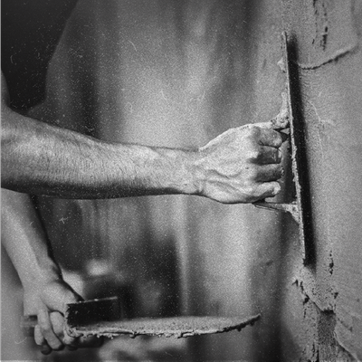 Person troweling wet plaster onto a wall with a hawk and plastering trowel