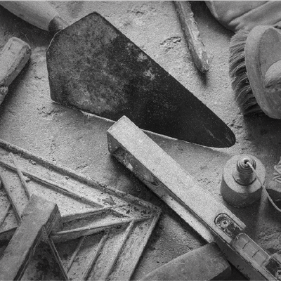 Assorted construction tools and materials scattered on a workbench in grayscale.