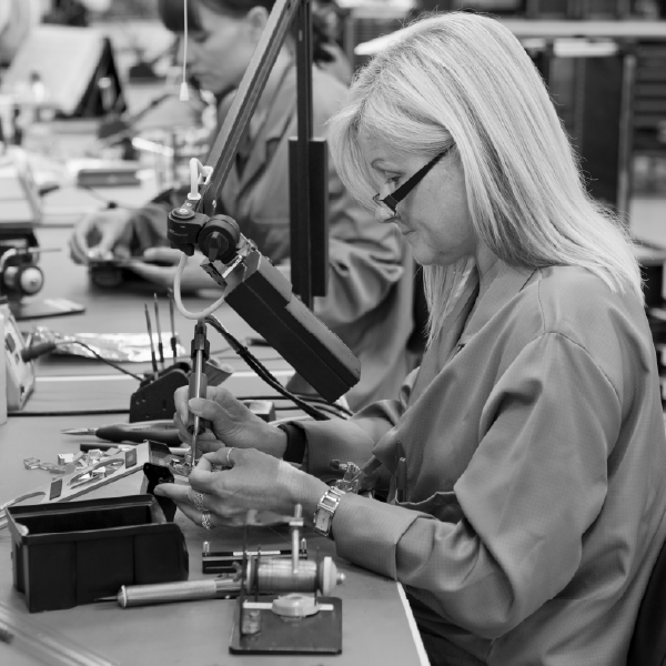 Technician working at an electronics bench, soldering components with tools and equipment nearby