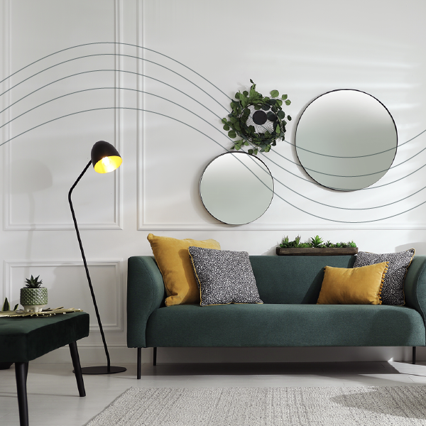 Modern living room with green sofa, black floor lamp, round mirrors, and decorative plants