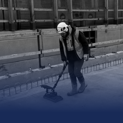 Person using a floor sander at a construction site, wearing a mask and safety vest.