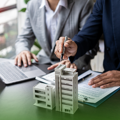 Businesspeople reviewing a miniature office building model beside a laptop and financial documents