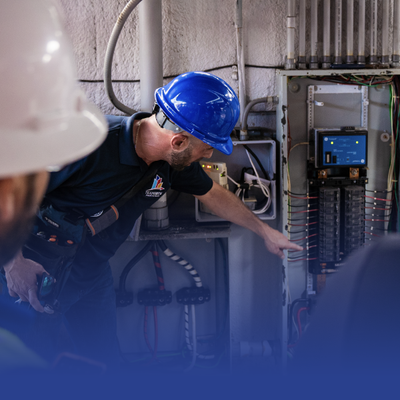 Technician in blue hard hat inspecting electrical control panel in an industrial setting