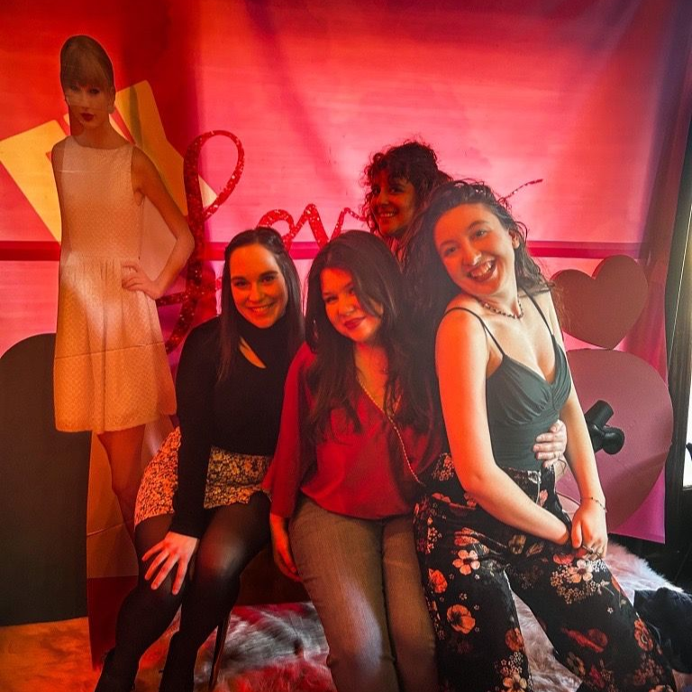 Four people posing in a pink-lit room with a mannequin in the background