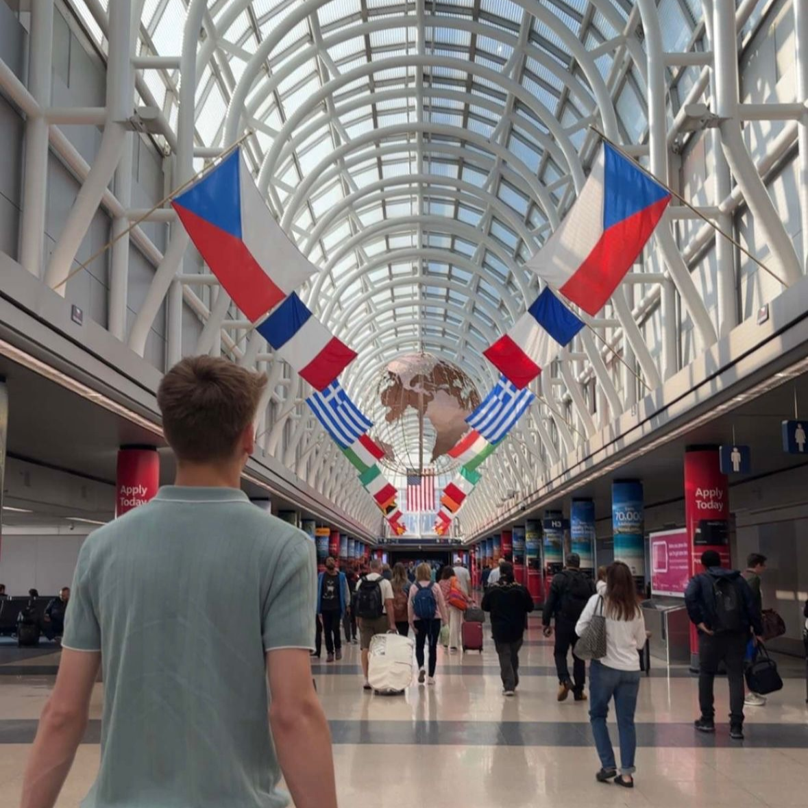 People walking through a bright glass-roofed concourse with red, white, and blue banners overhead