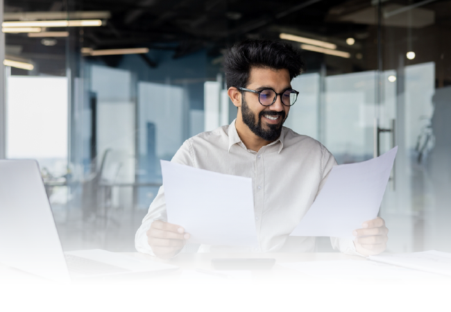 Man smiling at a desk, reviewing two documents in a modern office