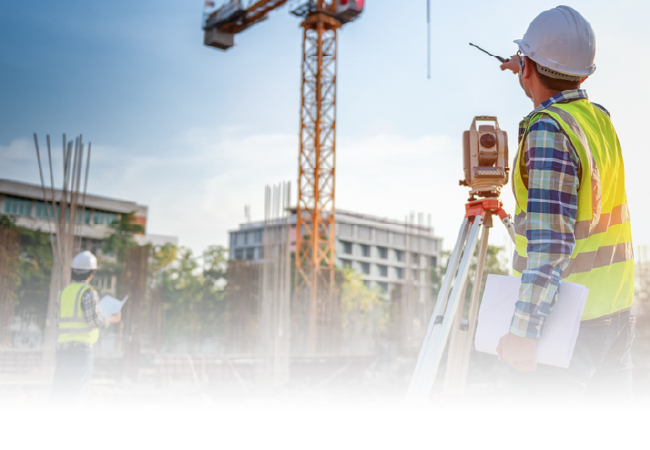Surveyor in hard hat checks construction site with tripod level and crane in background