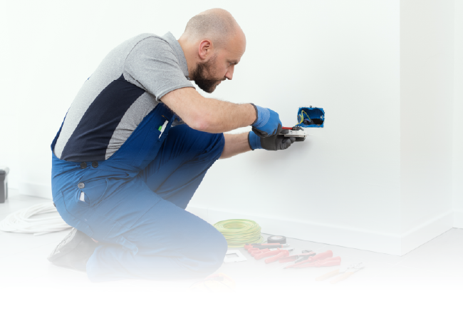 Painter crouched at a wall, applying white paint with a brush and tray nearby