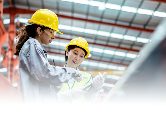 Two engineers in yellow hard hats reviewing plans in an industrial facility