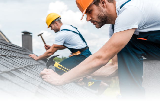 Two roofers in hard hats installing shingles on a rooftop