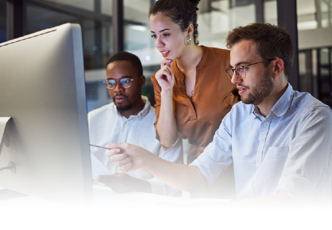 Three coworkers collaborating at a desk, looking at a computer screen in an office.