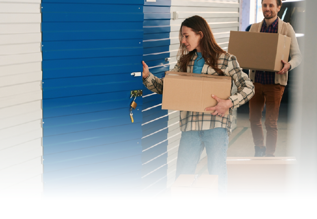 People carrying moving boxes through a hallway with blue storage doors