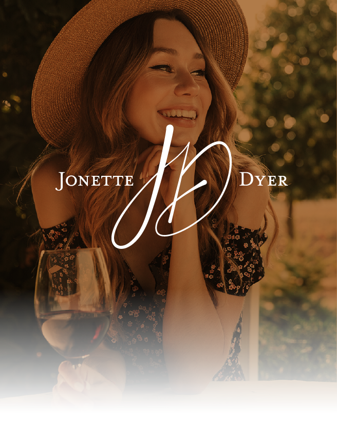 Woman smiling in a sunhat at an outdoor table, holding a wine glass, with “Jonette Dyer” text overlayed