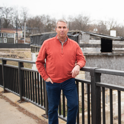 Man in a red jacket leaning on a railing by a waterfront on an overcast day