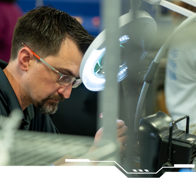 Technician wearing safety glasses works at a lit workstation in a workshop.