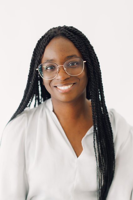 Smiling person with long braids and glasses in a white blouse against a light background