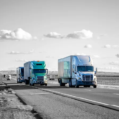 Two semi trucks driving on a highway under a cloudy sky.