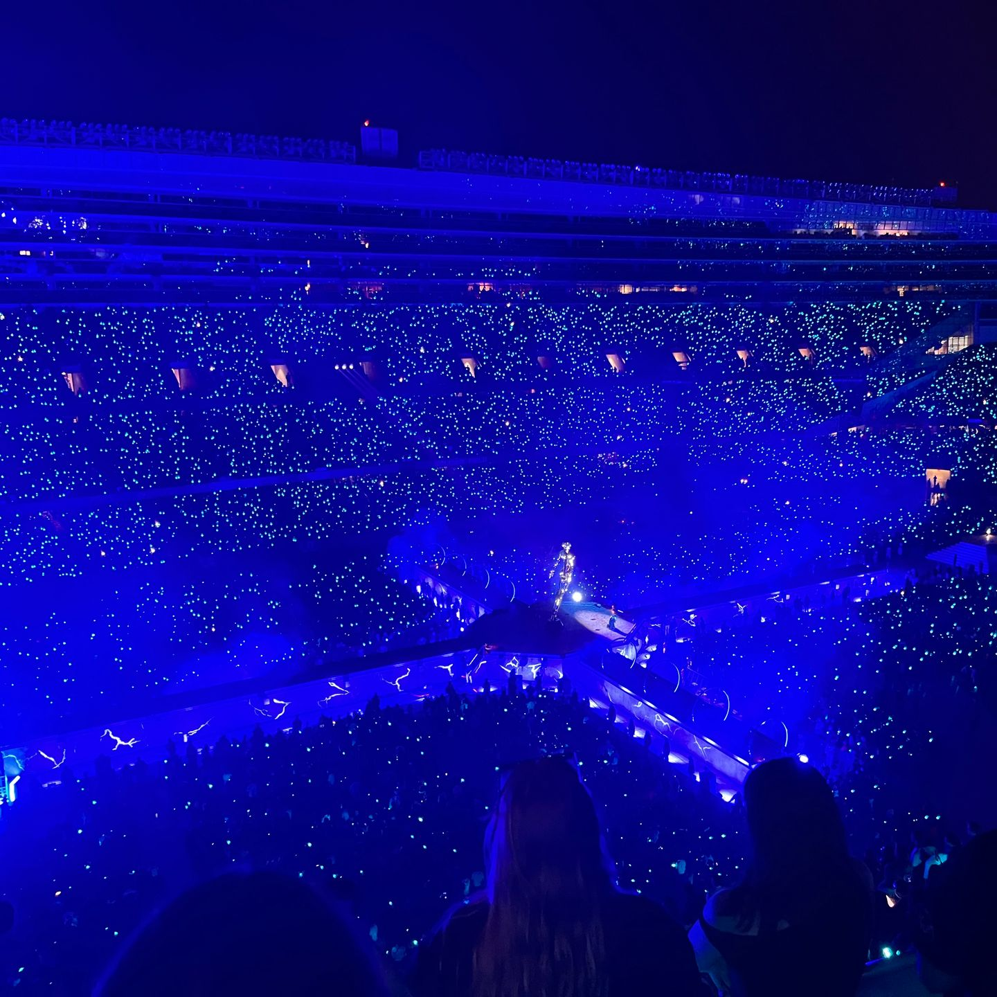 Blue-lit concert arena with a glowing stage and crowd lights filling the stadium