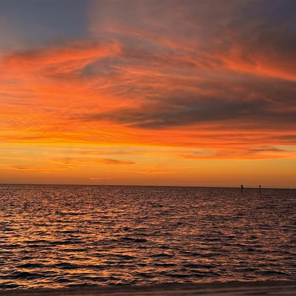 Orange sunset over a calm ocean with rippling water and dramatic clouds